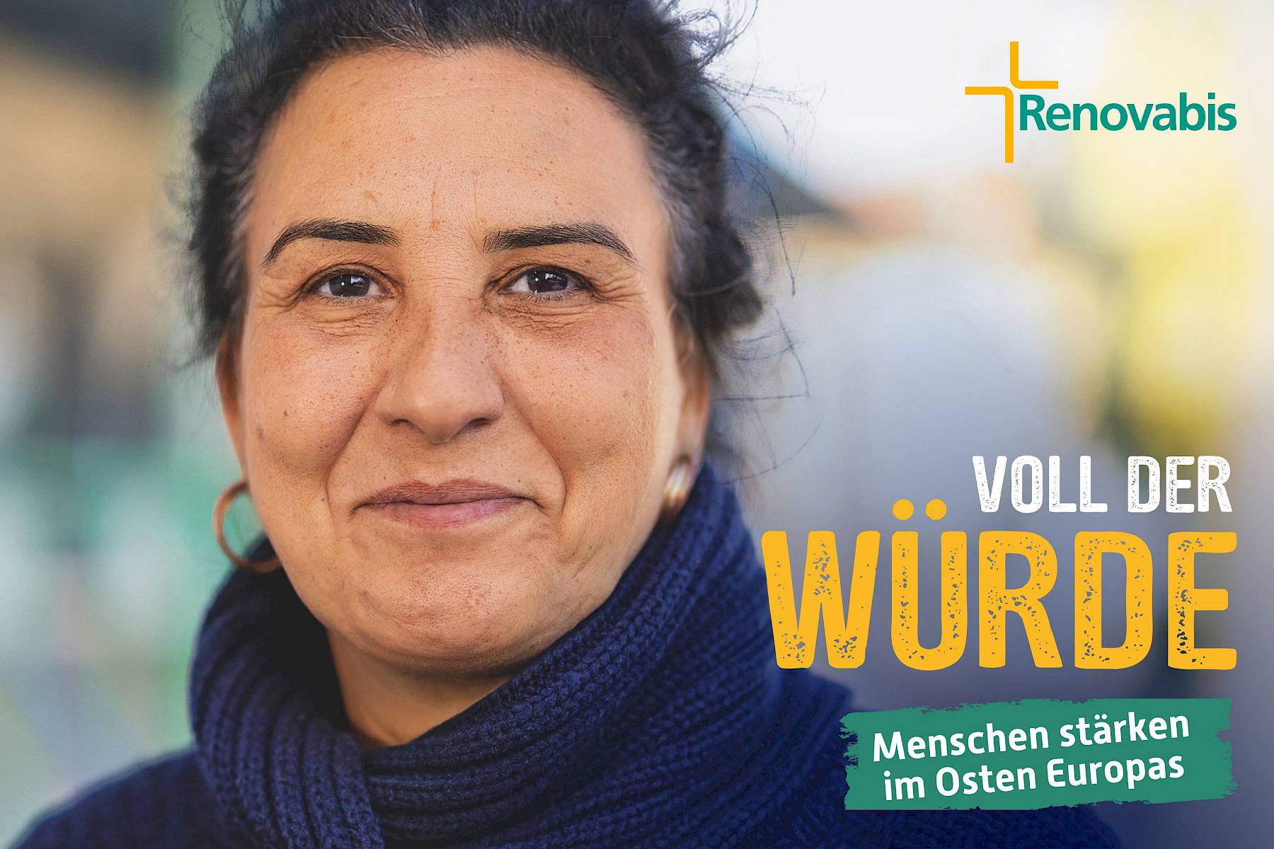 Das Foto zeigt eine Frau mit dunklen, lockigen Haaren, die zu einem lockeren Dutt gebunden sind. Sie blickt direkt in die Kamera und lächelt leicht. Sie trägt goldene Ohrringe und einen dunkelblauen, dicken Strickpullover. Das Gesicht wirkt ruhig und zugewandt. In der rechten unteren Bildecke steht in großen Buchstaben der Schriftzug „VOLL DER WÜRDE“ – das Wort „WÜRDE“ ist in kräftigem Gelb hervorgehoben. Darunter befindet sich ein grünes Textelement mit weißer Schrift: „Menschen stärken im Osten Europas“. Oben rechts ist das Renovabis-Logo zu sehen.
